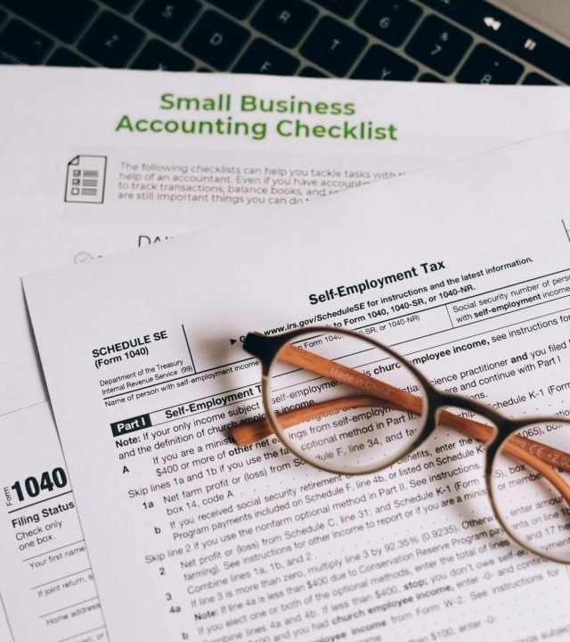 Close-up of tax forms and a small business accounting checklist on a laptop.